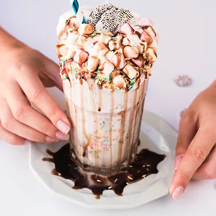 Loaded freak shake with whipped cream chocolate drizzle and toppings in a glass